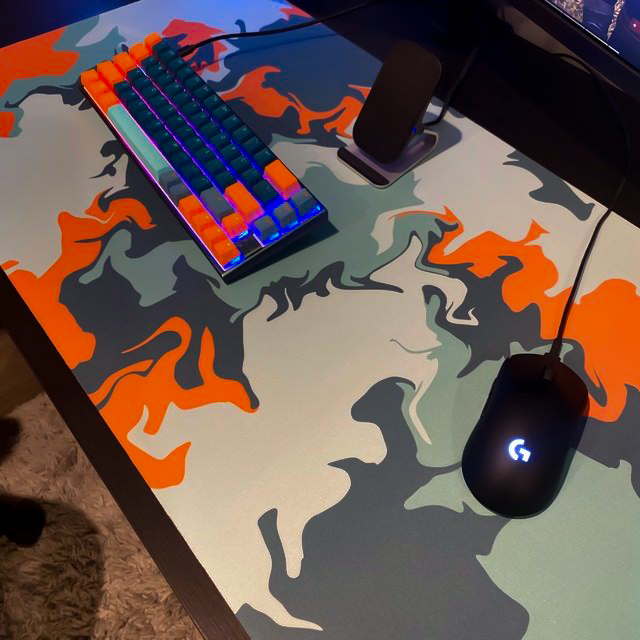 Custom desk mat printed with a gray and orange camo design under a mechanical keyboard and gaming mouse