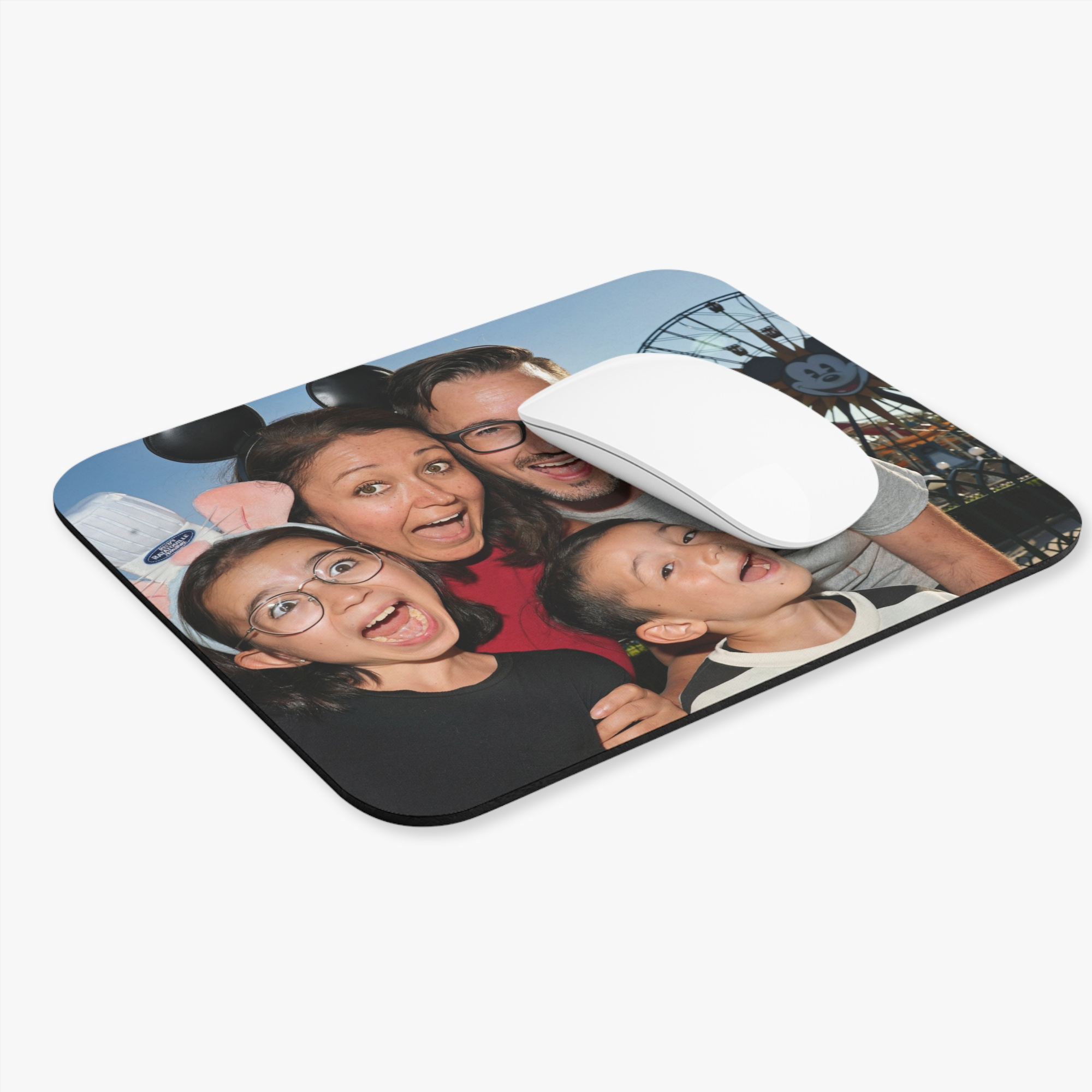 Custom mouse pad printed with a family photo from a theme park trip, shown at an angle with a white mouse